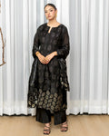 Woman wearing a black patterned outfit standing against a white curtain.