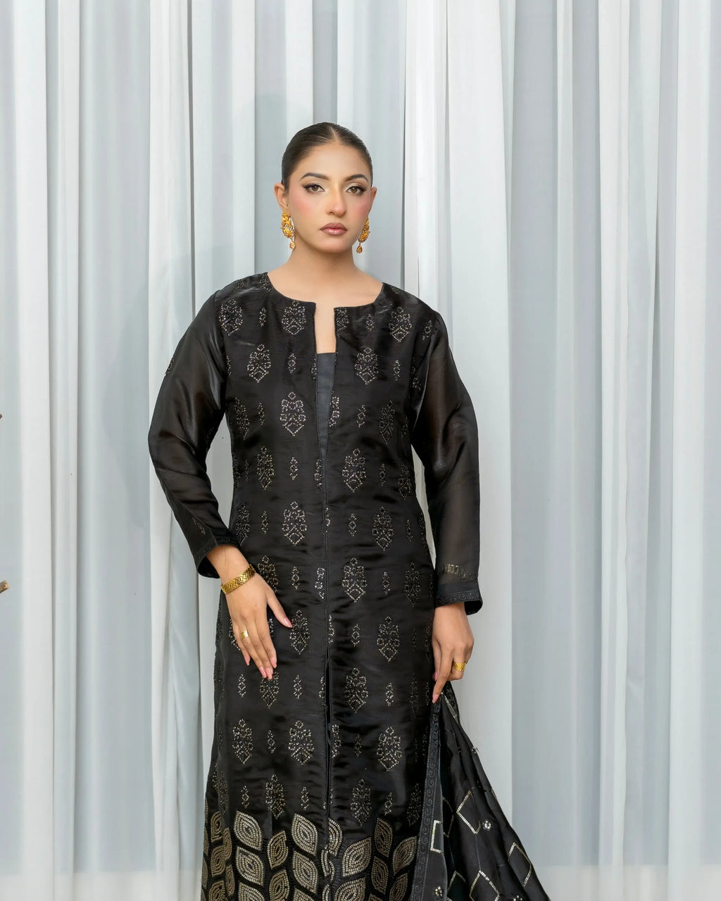 Woman wearing a black traditional outfit with a pattern against a white curtain background