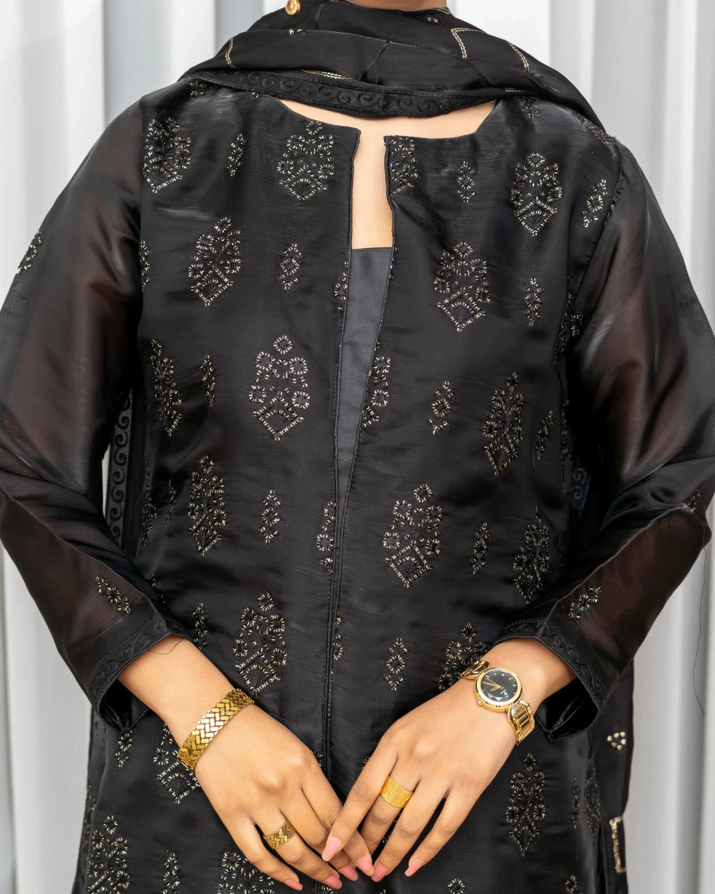 Black embroidered traditional outfit with gold jewelry on a white background