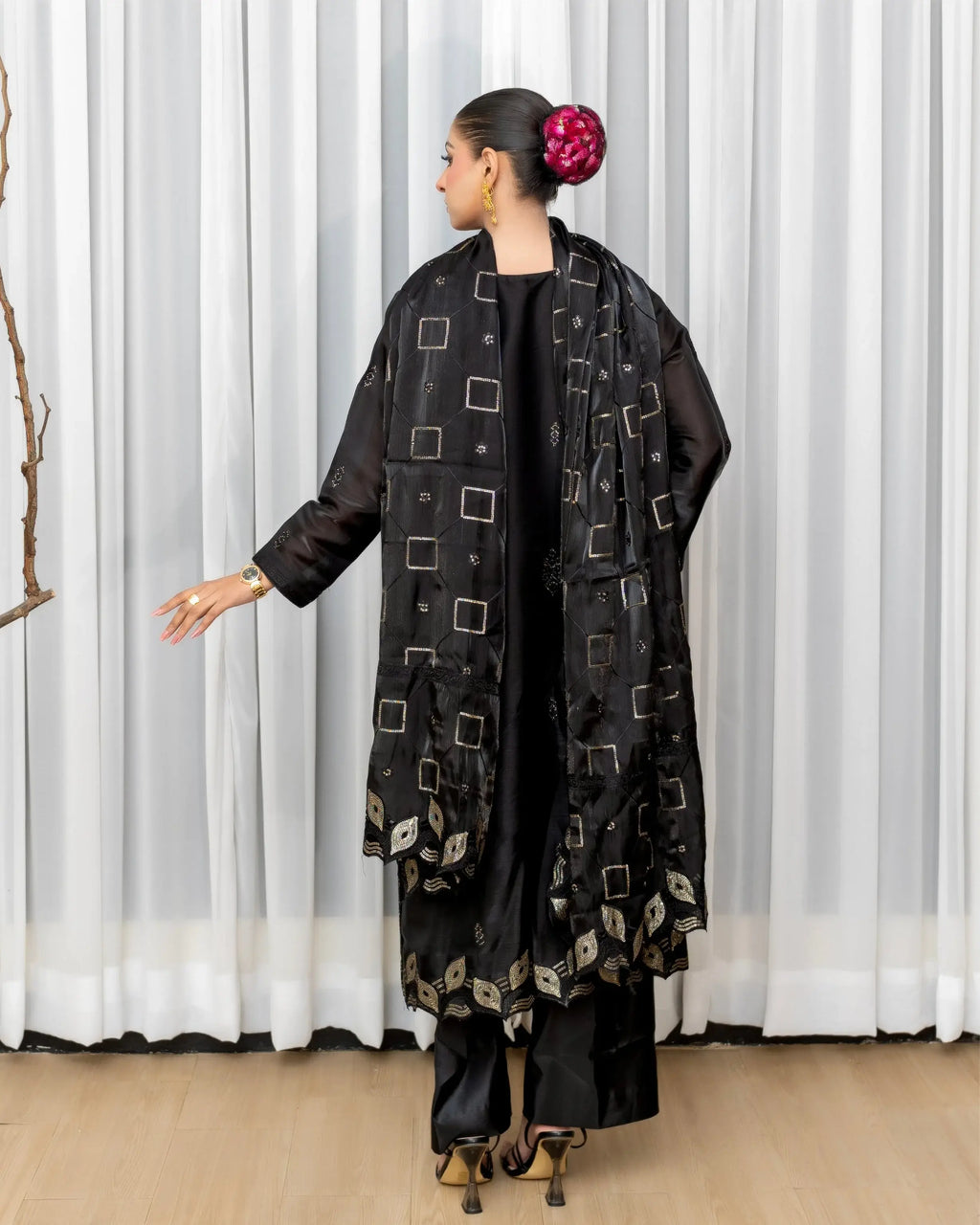 Woman wearing a black patterned outfit against a white curtain background