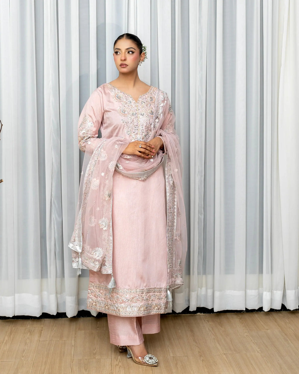 Woman in a pink traditional outfit with embroidery standing against a white curtain.