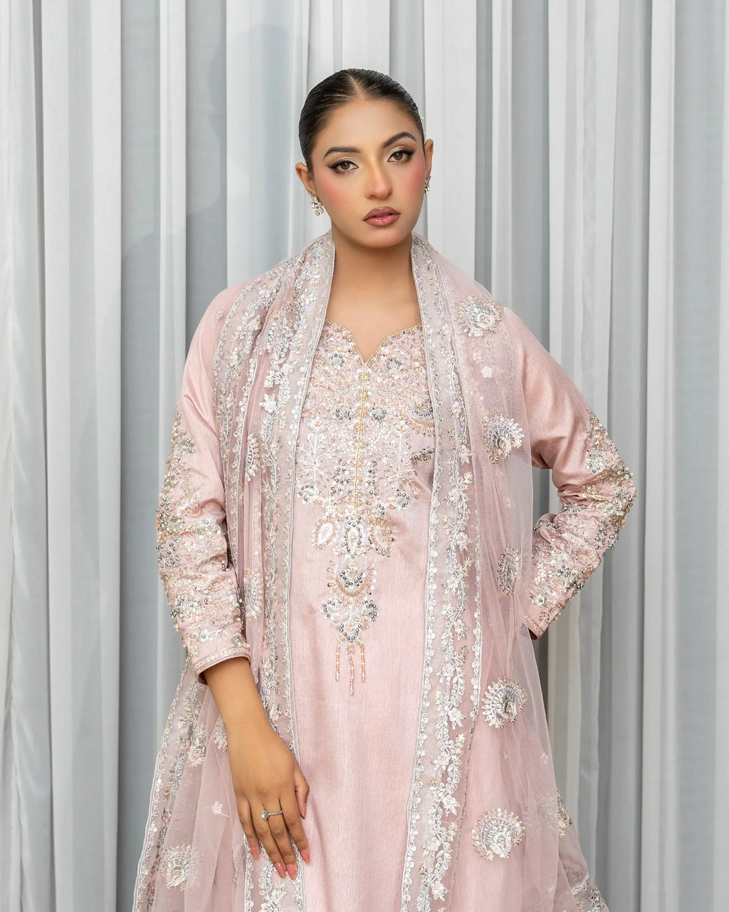 Woman wearing a light pink embroidered outfit against a gray curtain background