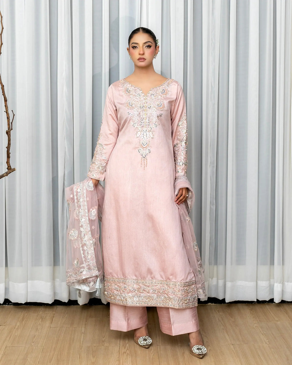 Woman wearing a pink embroidered outfit with a white curtain background