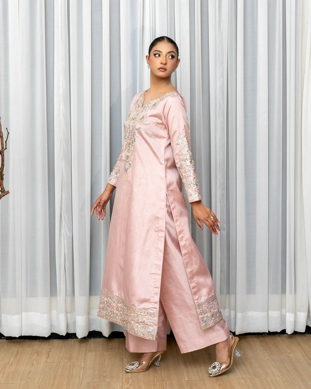 Woman wearing a pink traditional outfit with white embroidery against a white curtain background