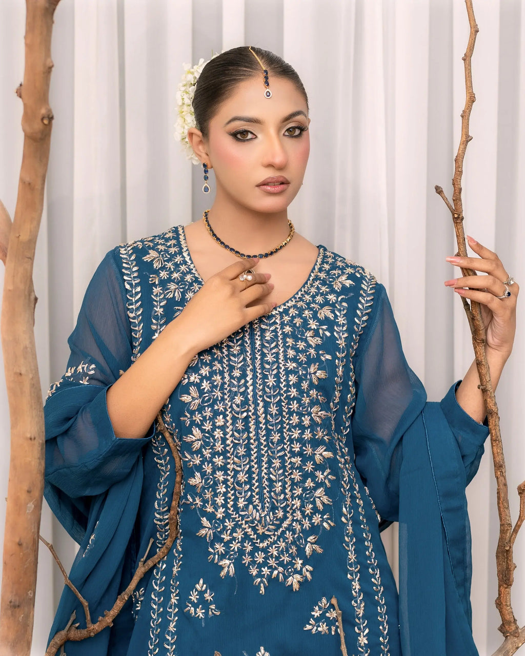 Woman wearing a blue embroidered traditional outfit with white curtains in the background