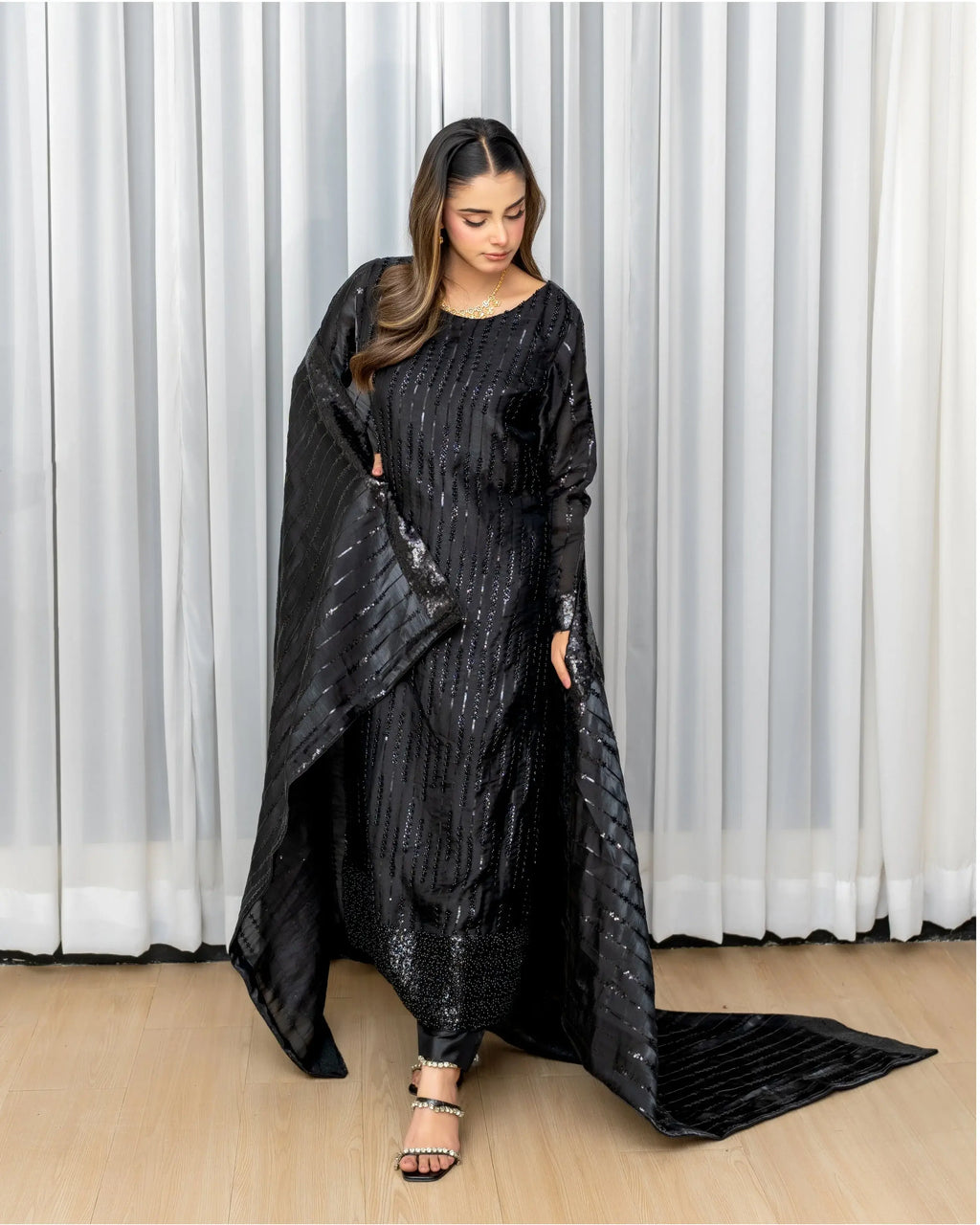 Woman wearing a black outfit with a long, flowing cape against a white curtain background