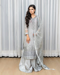 Woman wearing a light gray embroidered traditional outfit with a white curtain background