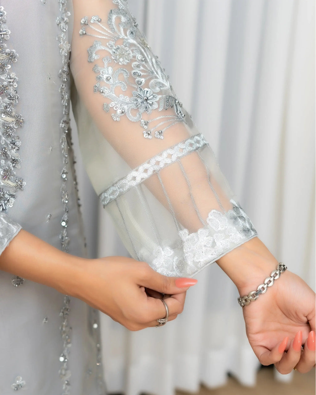 Close-up of a person wearing a silver embroidered sleeve with floral details against a neutral background.