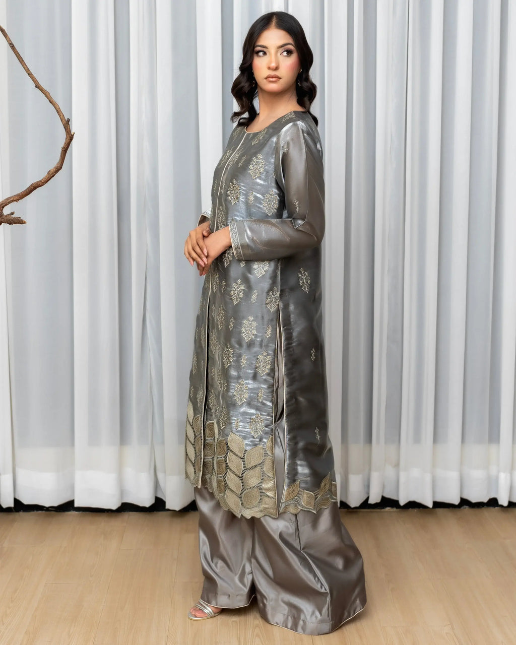 Woman wearing a silver embroidered traditional outfit against a white curtain background