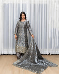 Woman wearing a silver embroidered traditional outfit with a long scarf against a white curtain background
