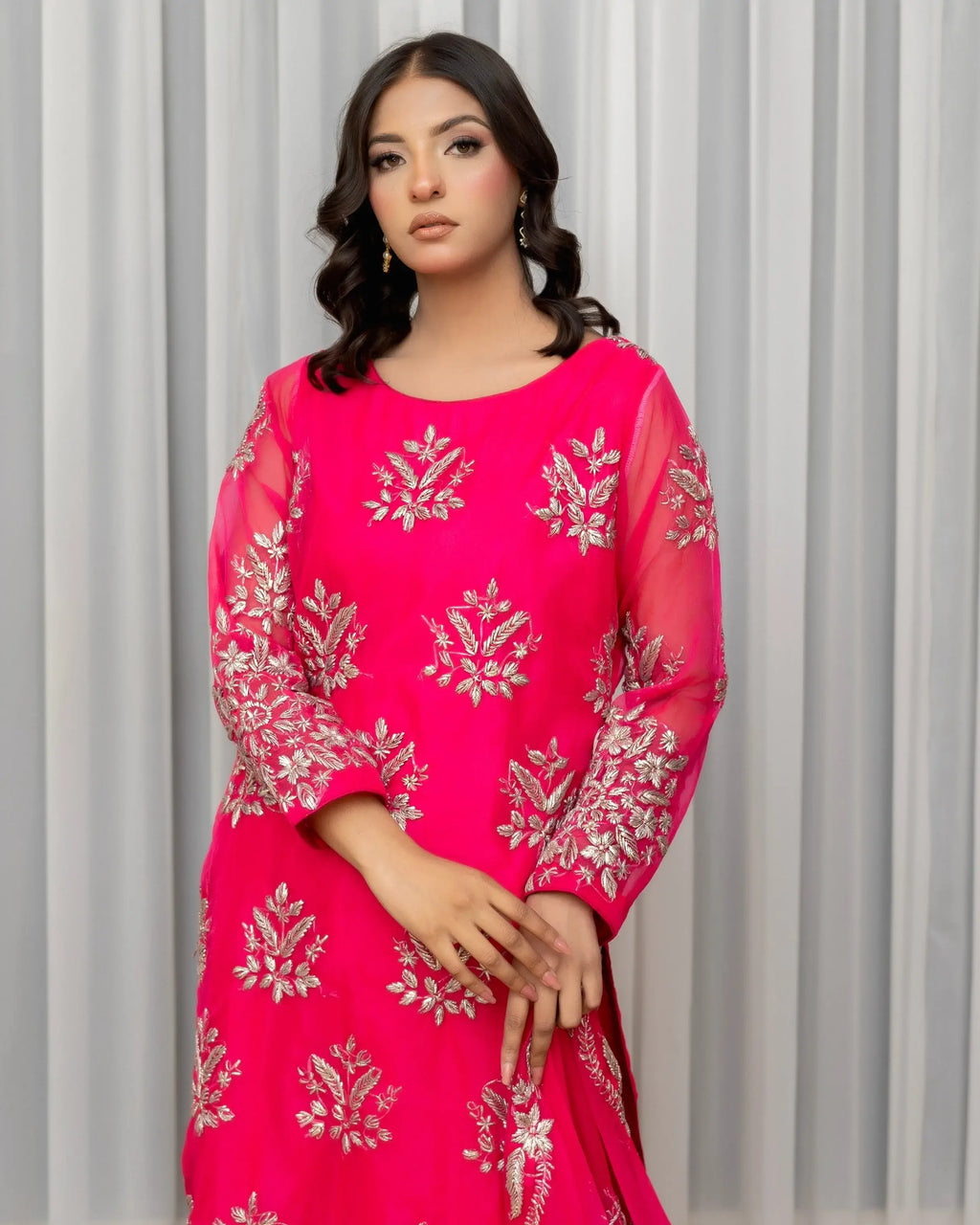 Woman wearing a pink traditional outfit with silver embroidery against a gray curtain background