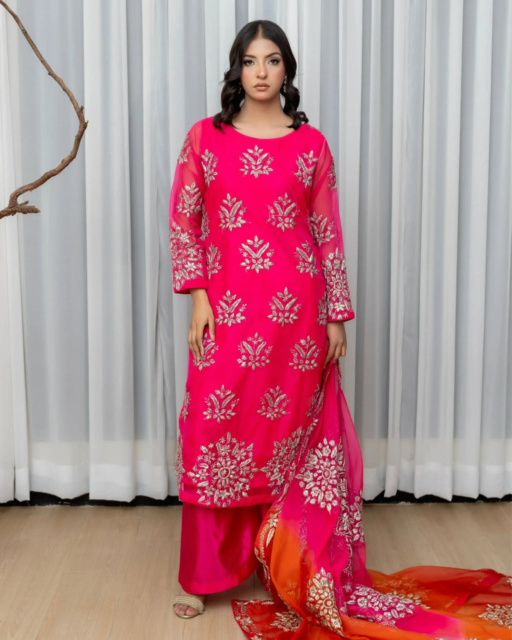 Woman wearing a pink traditional outfit with a saree in a room with white curtains.