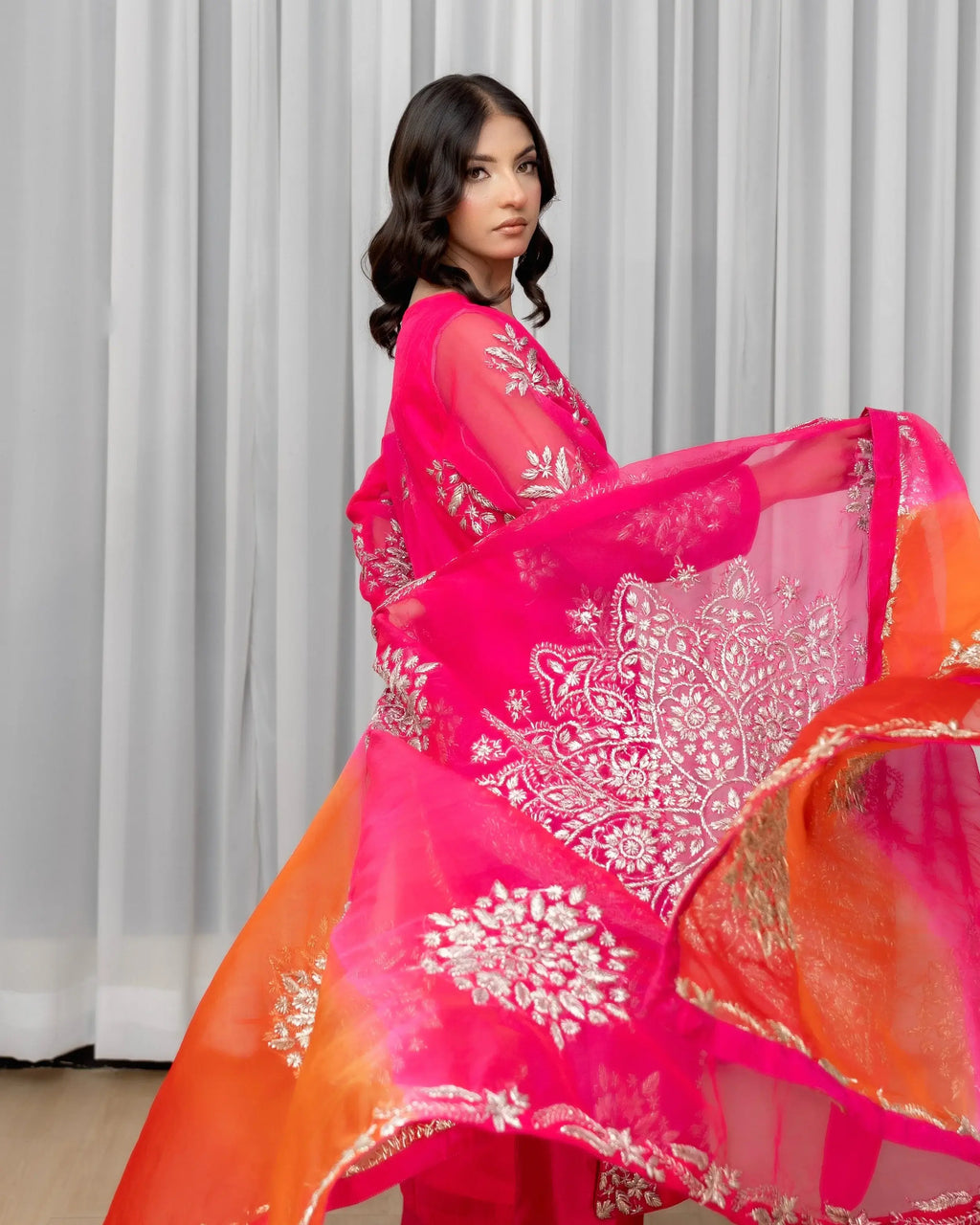 Woman wearing a pink and orange traditional outfit with white patterns against a neutral background