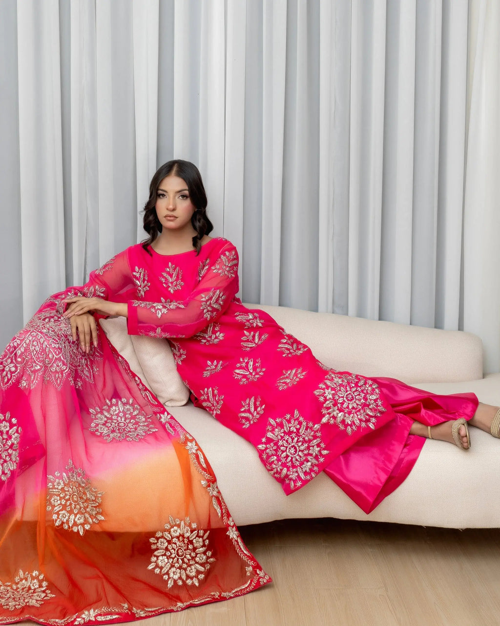 Woman in a pink and orange traditional outfit sitting on a couch with a neutral background