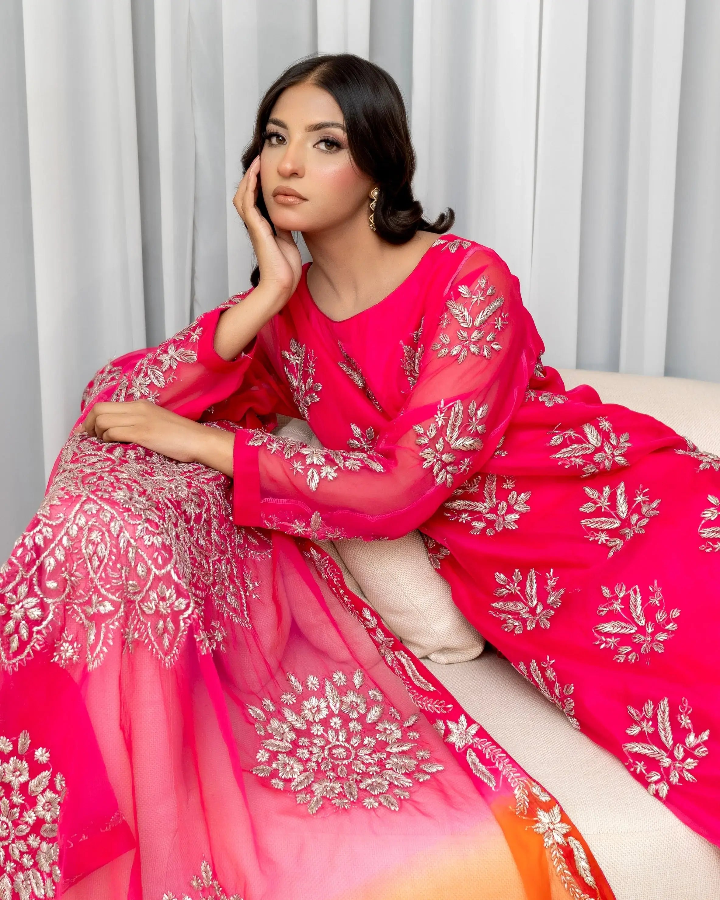 Woman in a pink traditional outfit with white embroidery sitting on a white couch.