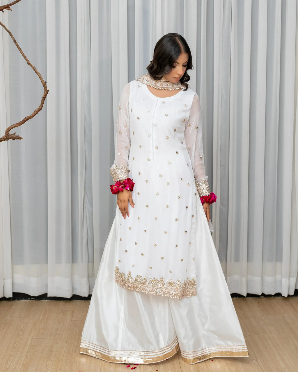 Woman wearing a white traditional outfit with gold embroidery against a striped curtain background
