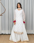 Woman wearing a white embroidered traditional outfit with red bangles against a light curtain background