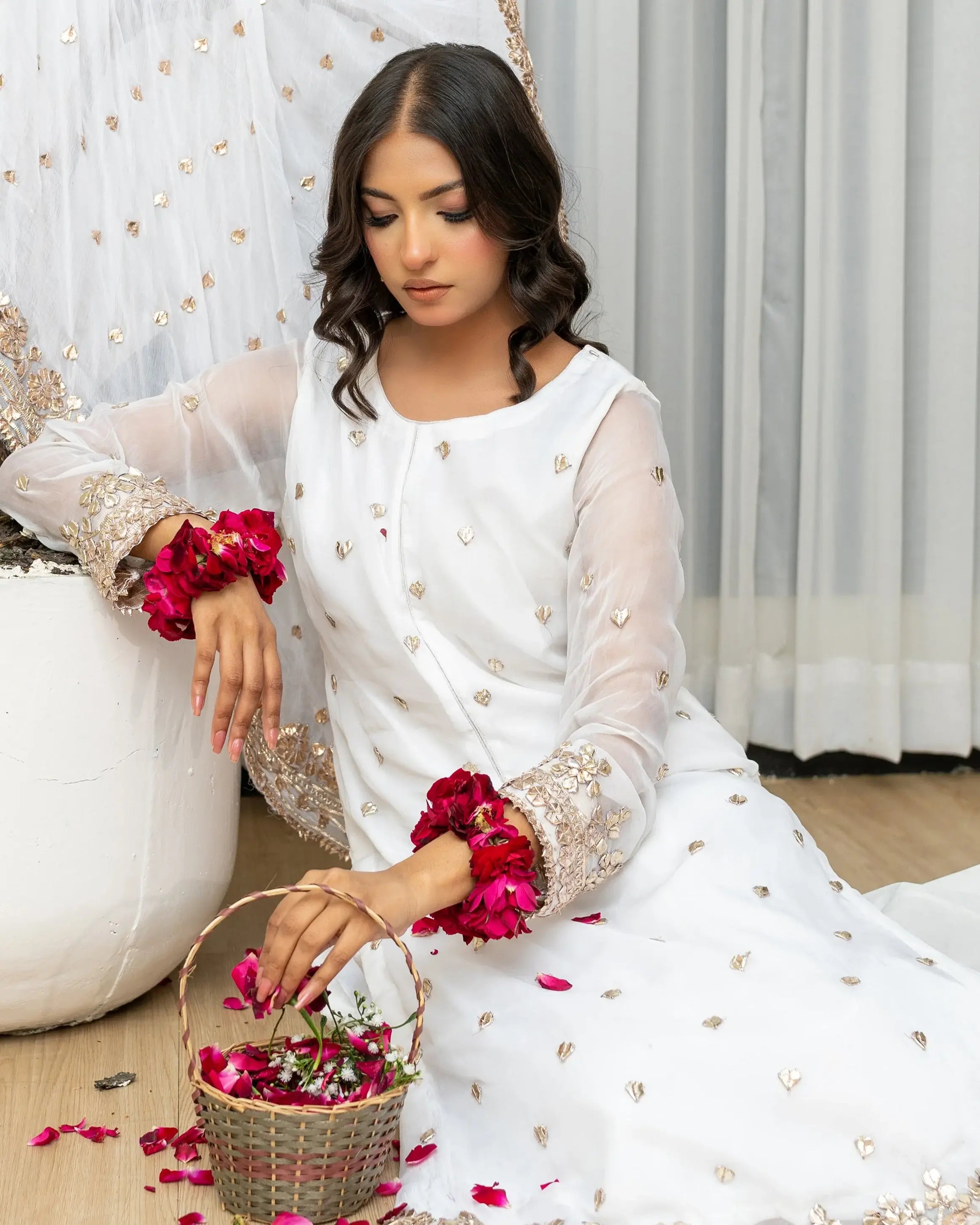 Woman in a white traditional outfit with floral decorations, sitting on the floor with a pumpkin and basket of flowers.