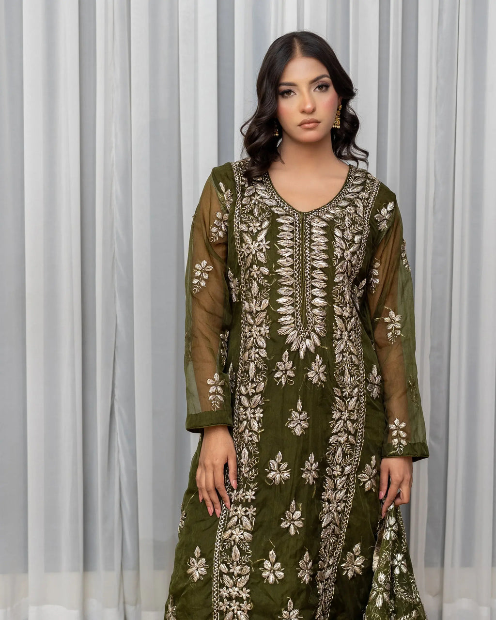 Woman wearing a green embroidered dress against a white curtain background