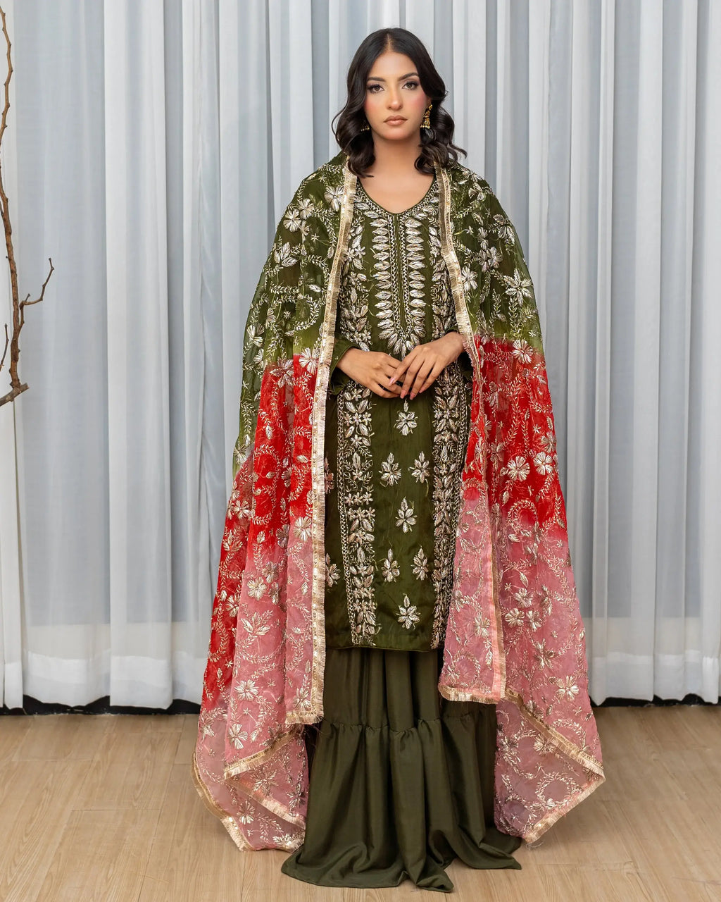 Woman wearing a traditional outfit with a green and red dupatta against a white curtain background