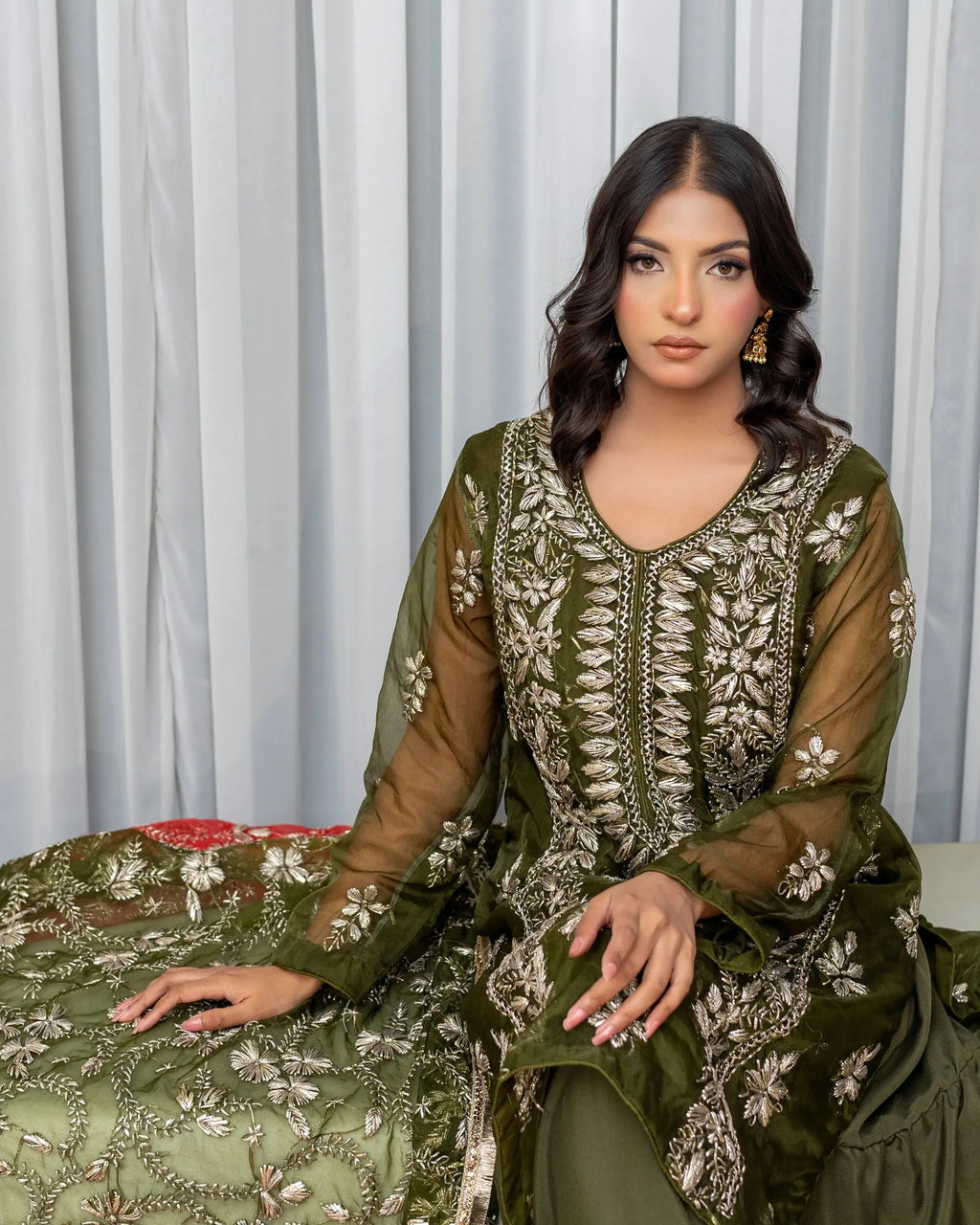 Woman wearing a green embroidered traditional outfit against a light curtain background