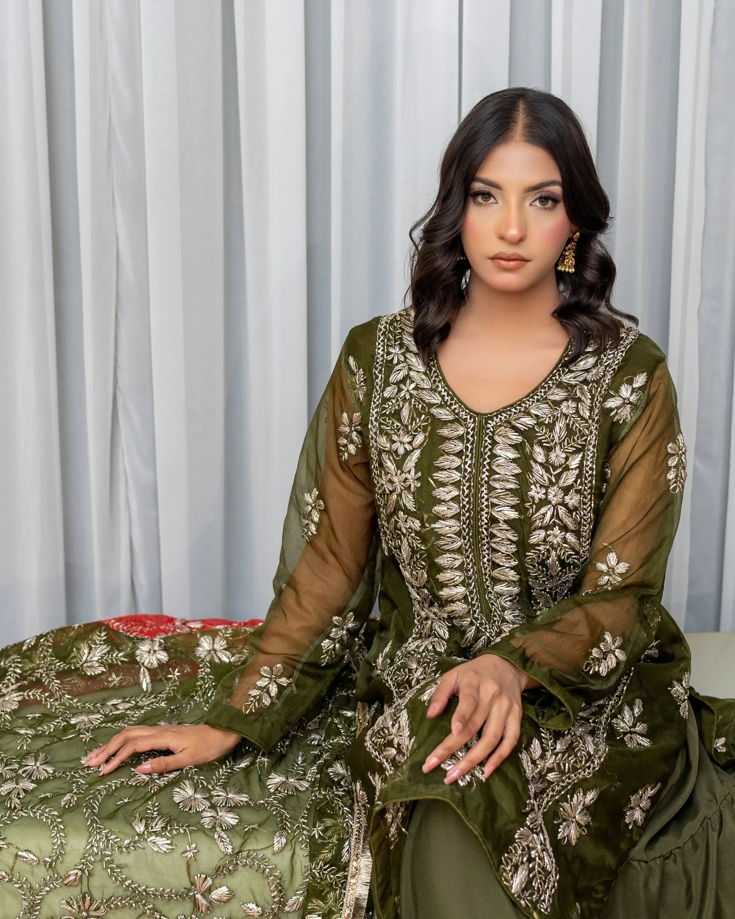 Woman wearing a green embroidered traditional outfit against a light curtain background