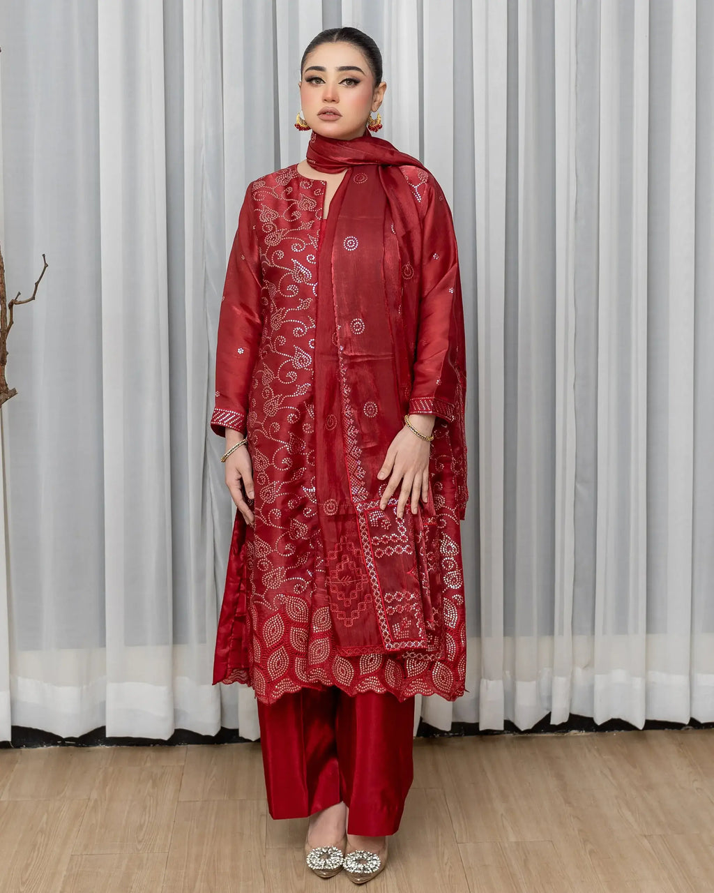 Woman wearing a red traditional outfit with intricate patterns against a white curtain background