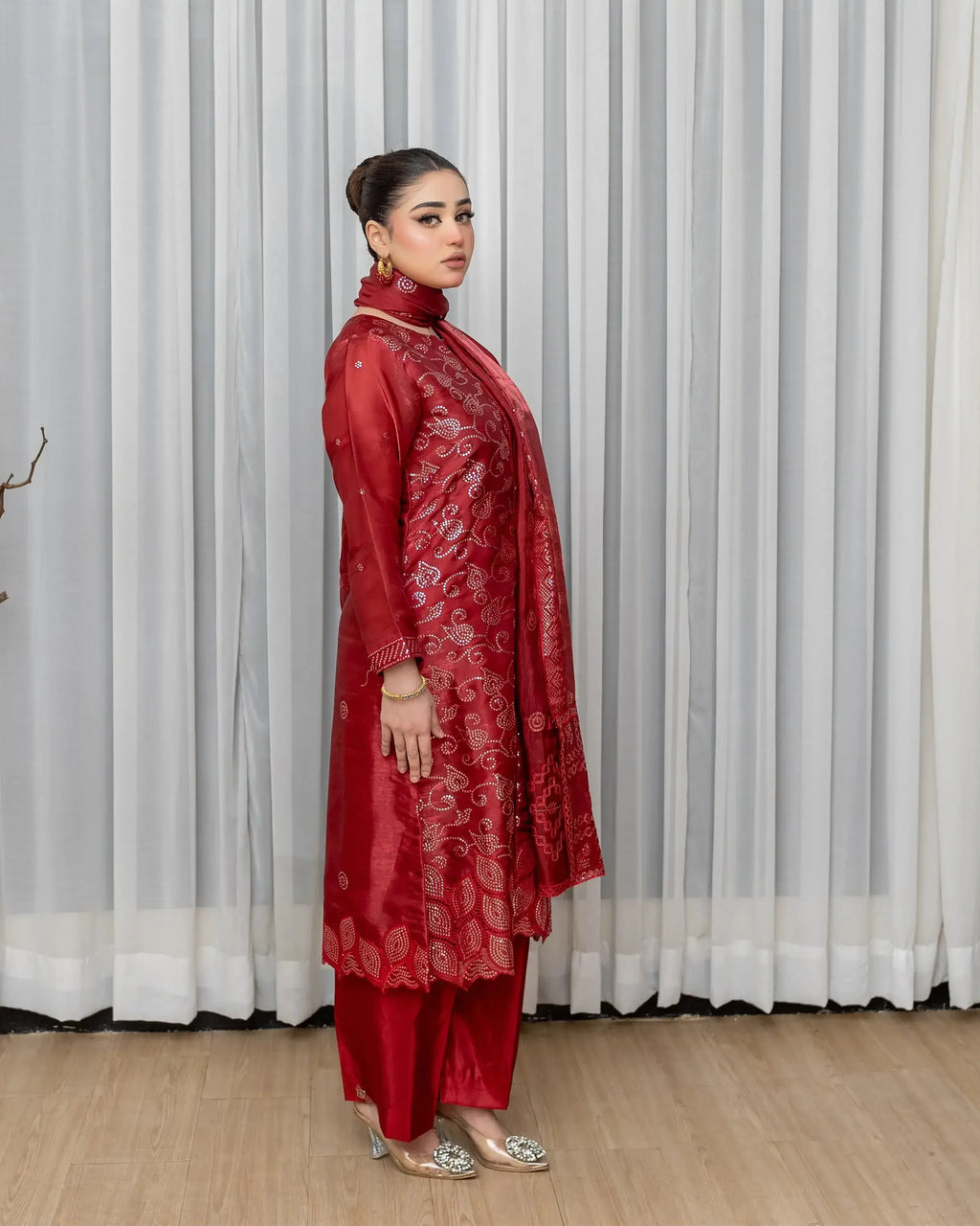 Woman wearing a red traditional outfit standing in front of white curtains.