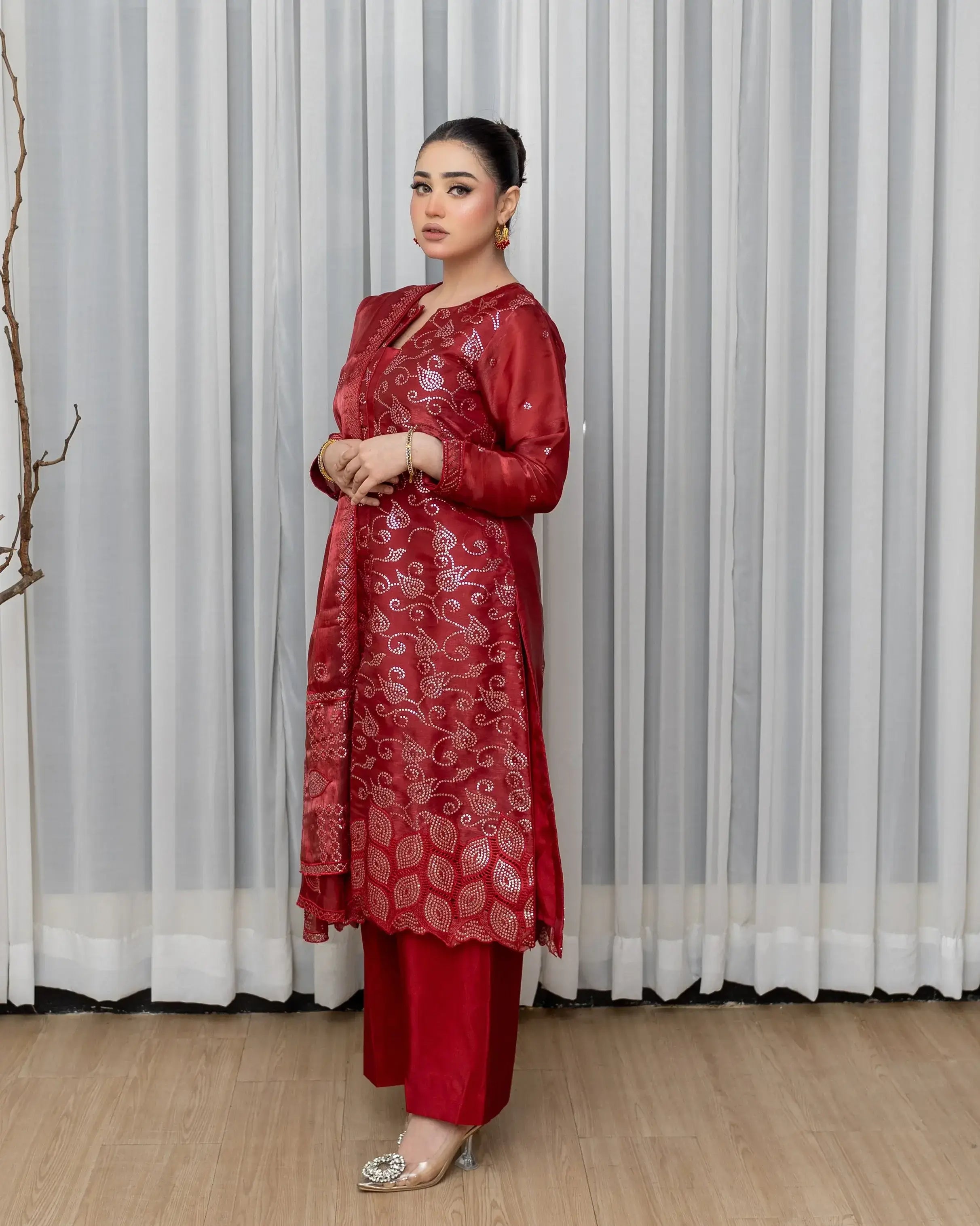 Woman wearing a red traditional outfit with intricate patterns against a white curtain background
