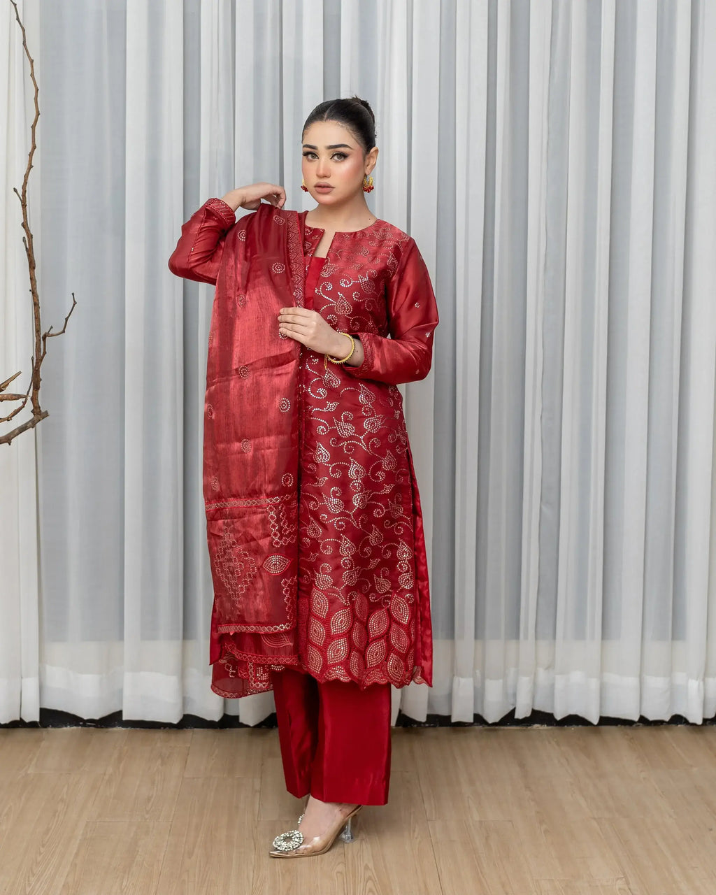 Woman wearing a red traditional outfit with a matching dupatta against a white curtain background