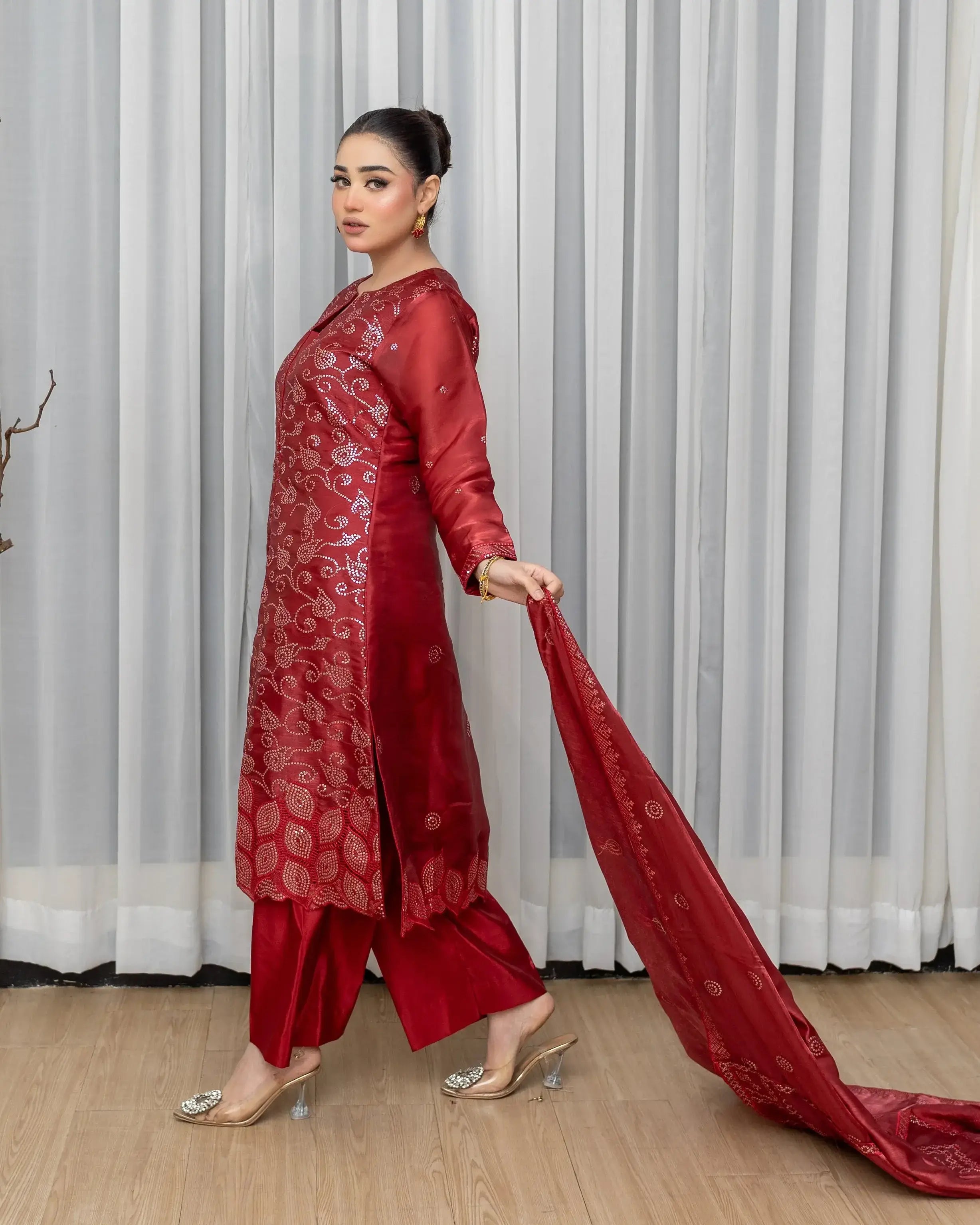 Woman in a red traditional outfit holding a long scarf against a white curtain background