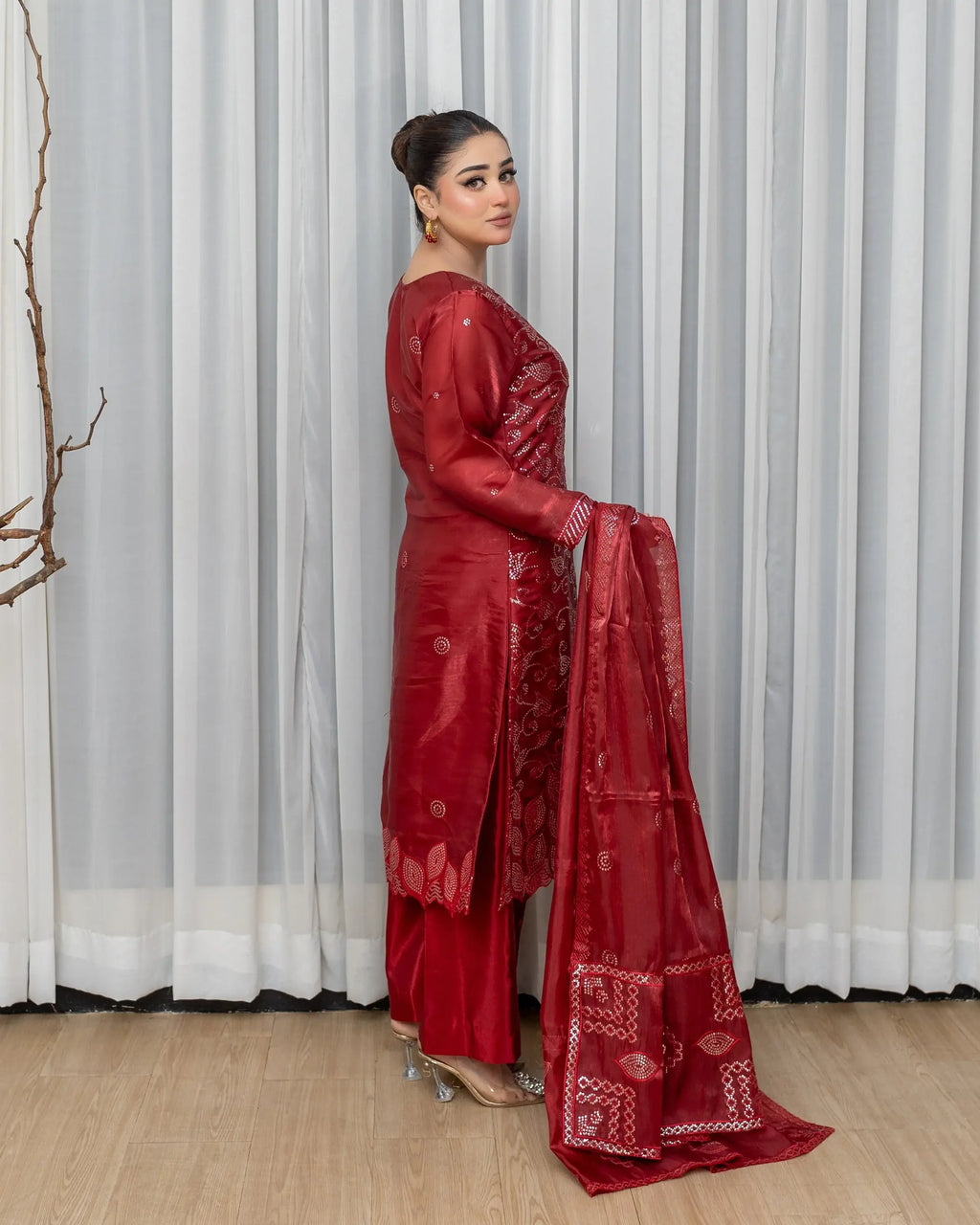 Woman in a red saree standing against a white curtain