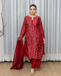 Woman wearing a red traditional outfit with a matching dupatta against a white curtain background