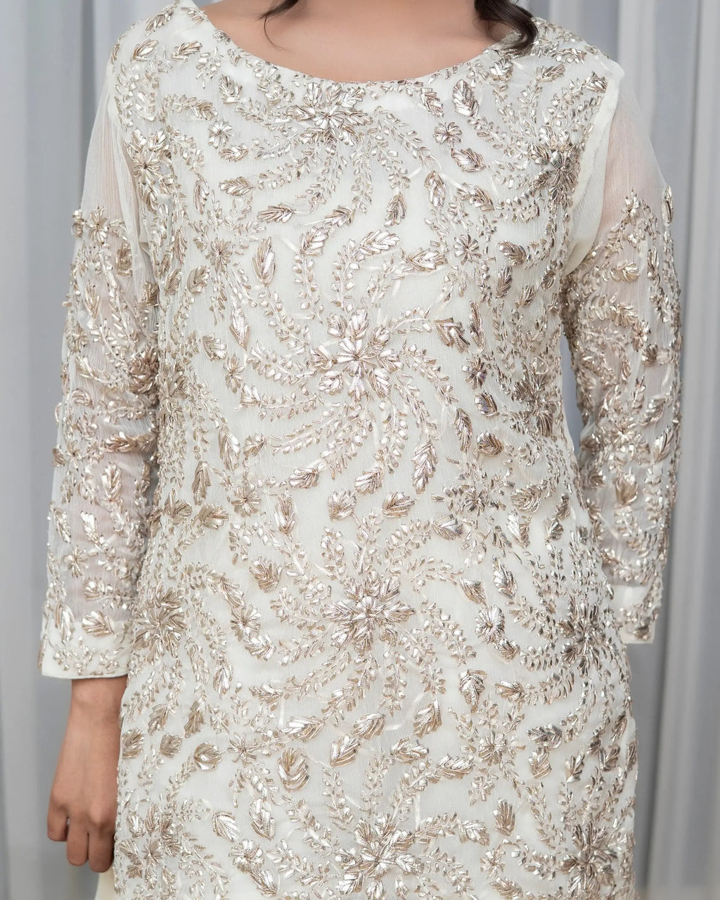 White dress with gold embroidery against a gray background