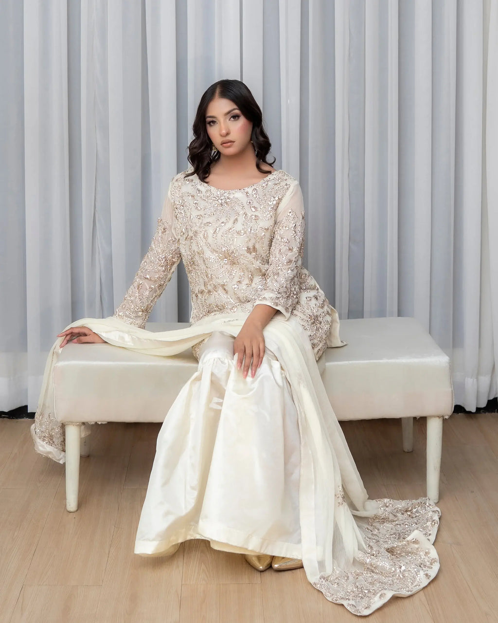 Woman in a white lace outfit sitting on a bench with a gray curtain background