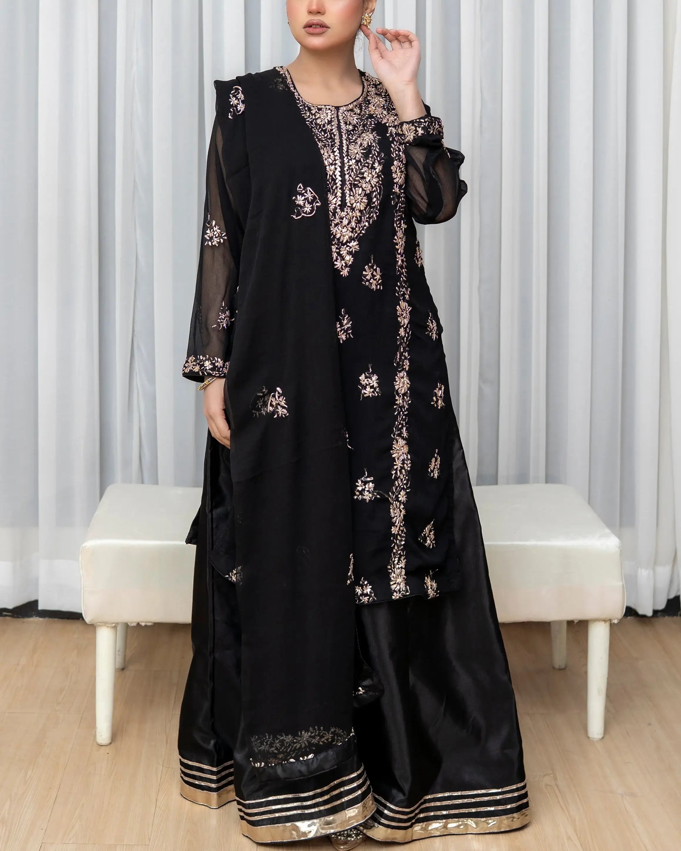 Woman wearing a black embroidered outfit with a white curtain background