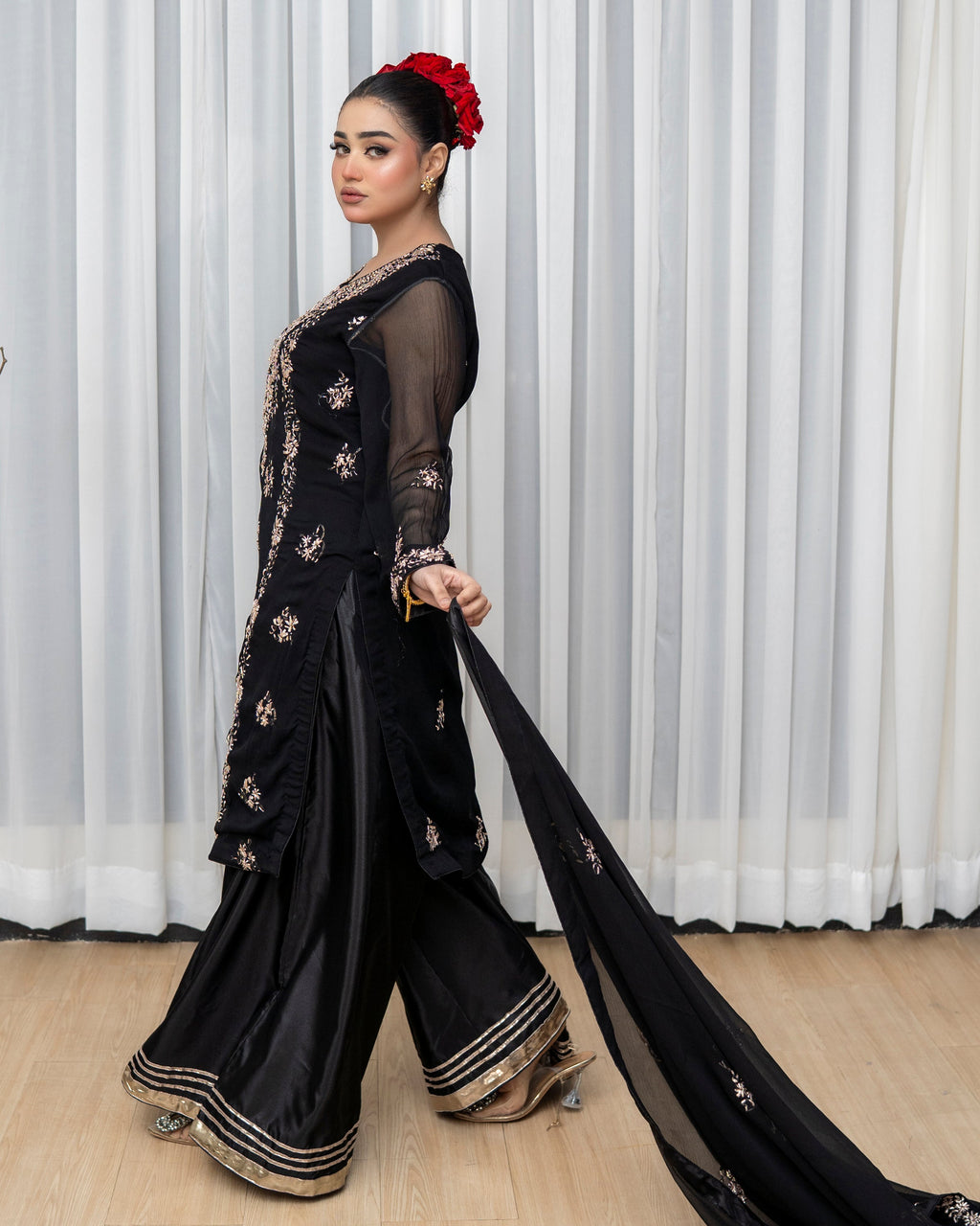 Woman in a black saree with gold details against a white curtain background