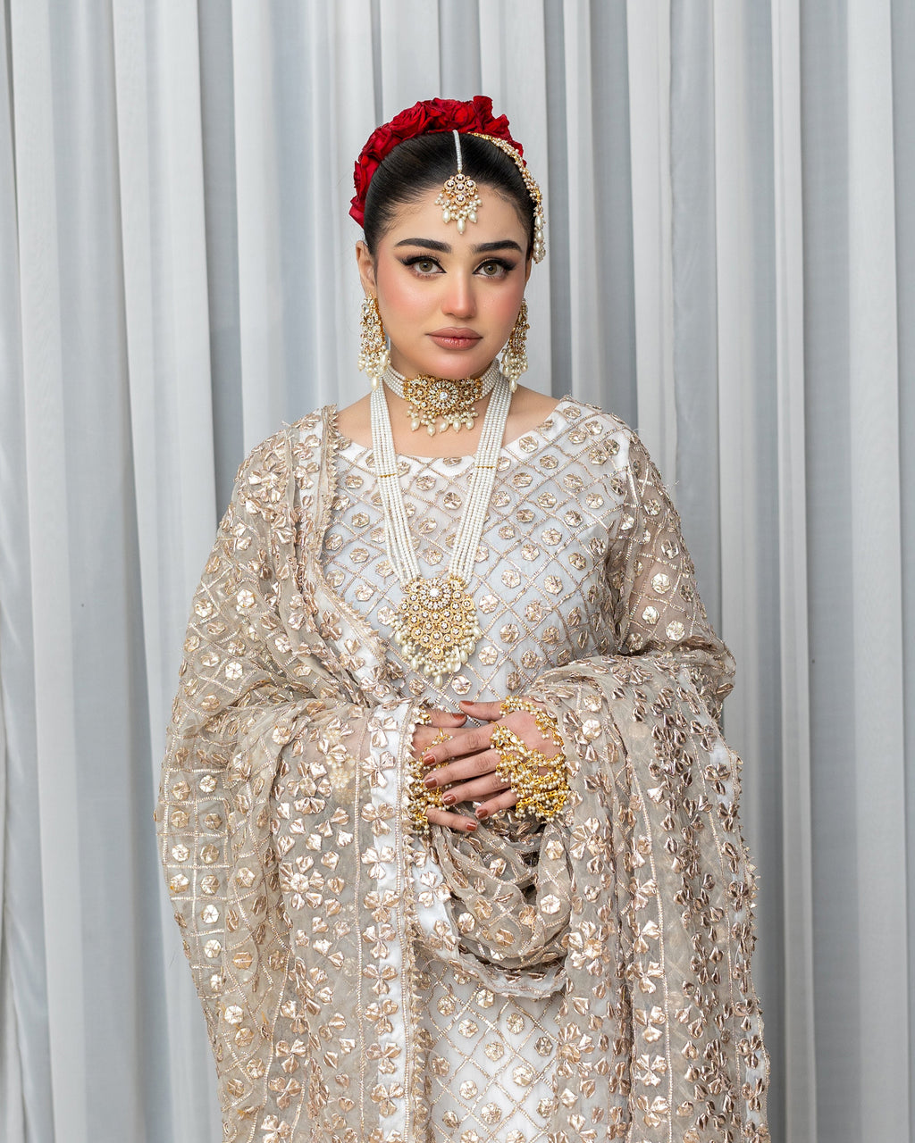 Woman in traditional embroidered outfit with jewelry against a gray curtain background