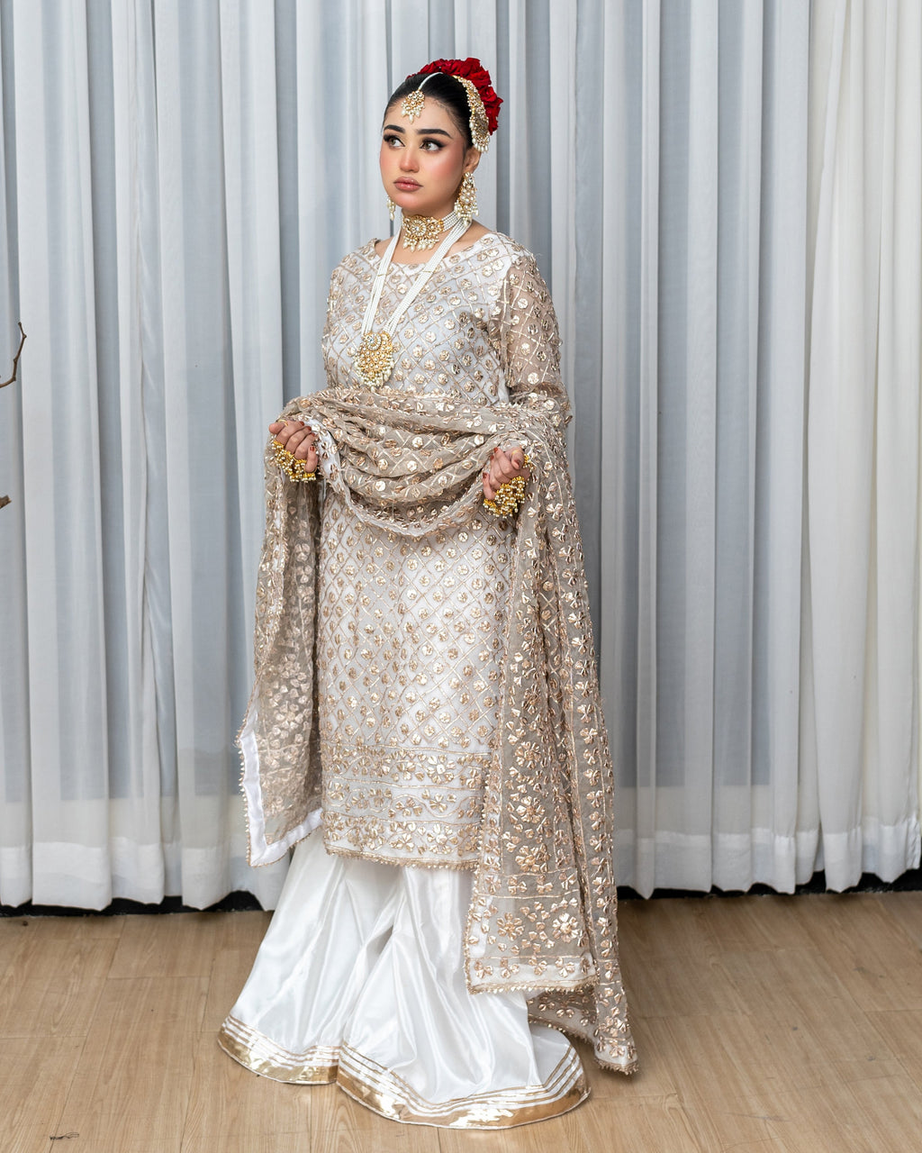 Woman in traditional embroidered outfit with a red headpiece against a white curtain background
