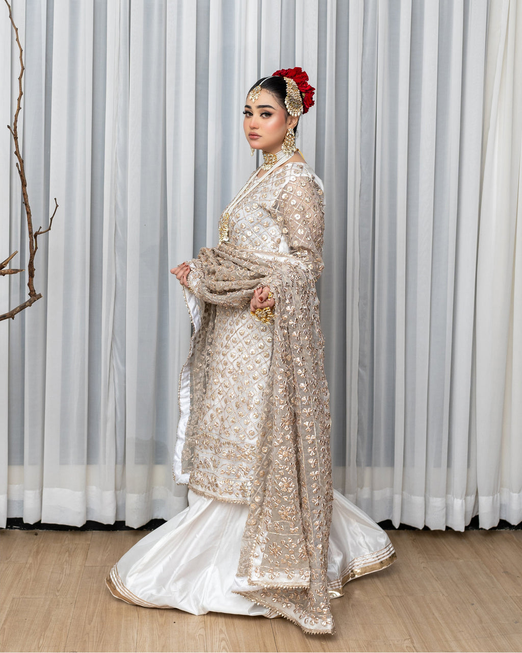 Woman in a traditional outfit with gold and white patterns against a neutral background
