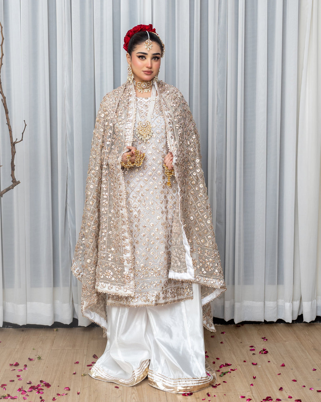 Woman in traditional attire with a gold embroidered shawl against a white curtain background