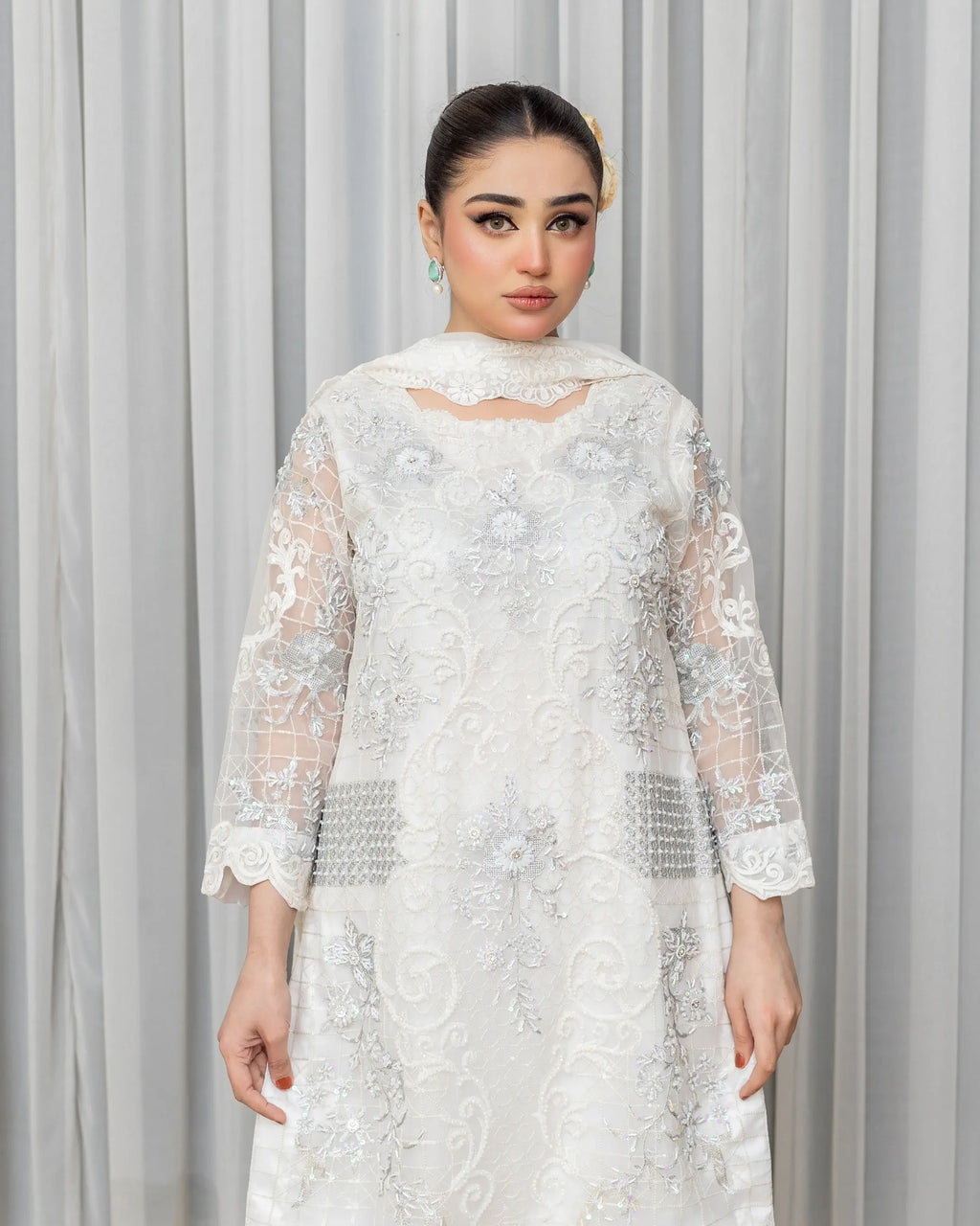 Woman wearing a white embroidered dress against a gray curtain background