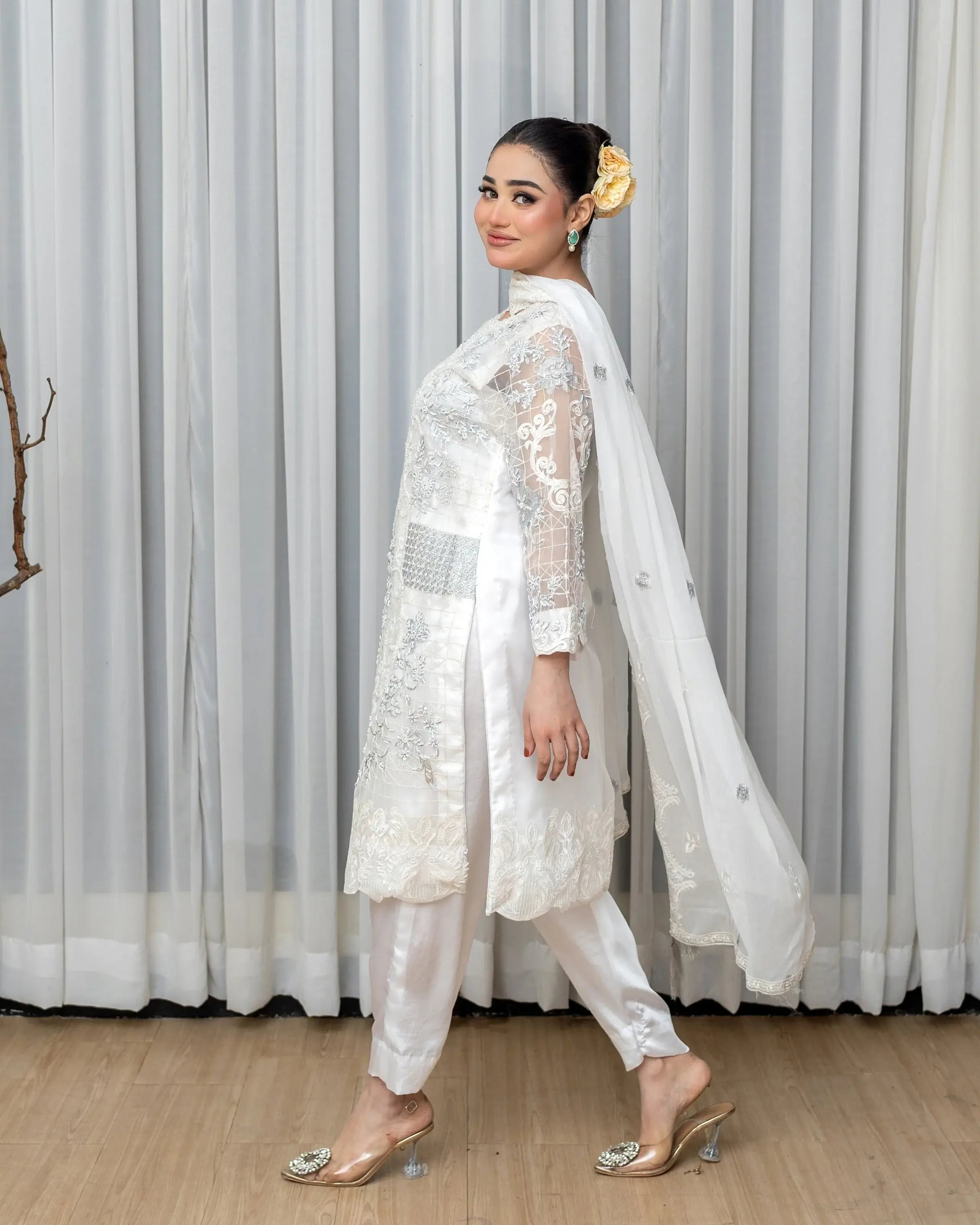 Woman in a white traditional outfit standing against a striped curtain.
