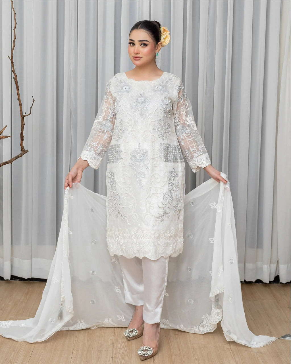 Woman wearing a white embroidered outfit with a sheer dupatta against a neutral background